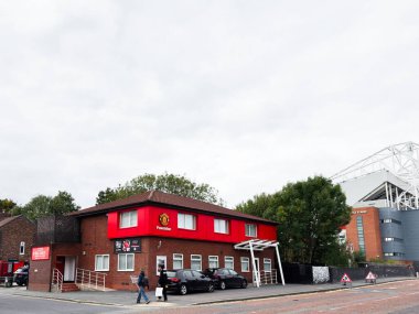 Manchester, İngiltere - 30 Eylül 2025: Manchester, İngiltere 'de yayalar ve park halindeki arabaların bulunduğu bir stadyumun yakınındaki Kızıl Vakıf binası.