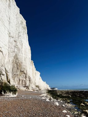 Beyaz tebeşir uçurumları Sussex kıyısındaki berrak mavi suyun yanında çakıllı bir plajın üzerinde kule gibi duruyor..