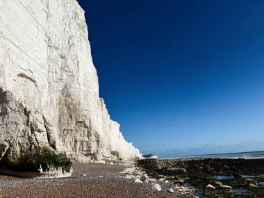 Kıyı boyunca tebeşir kayalıkları, kumlu bir sahil, uzakta deniz, ve parlak, berrak gökyüzü..