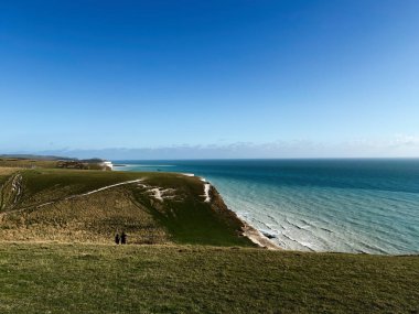 Seven Sisters Kayalıkları 'nda yeşil yamaçlar ve mavi deniz ufkunun bulunduğu sakin bir deniz manzarası..