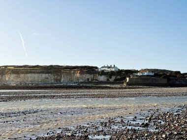 Sahil boyunca kayalık evlerin bulunduğu sakin bir sahil manzarası berrak mavi bir gökyüzünün altında.