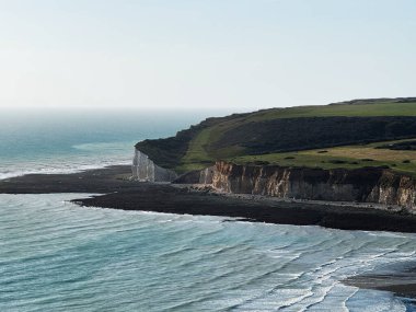 Sahilde beyaz kayalıklar, yeşil alanlar ve mavi deniz bulunan dramatik kıyı manzarası..