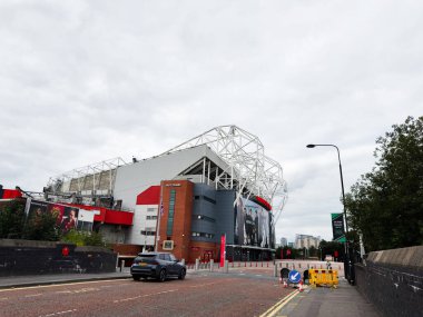 Manchester, İngiltere - 30 Eylül 2025: Manchester 'da büyük çağdaş bir stadyum, kırmızı tuğla aksanlı ve çevresindeki yol manzaralı.