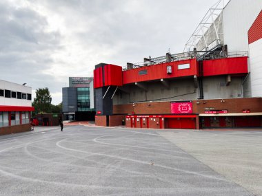 Manchester, İngiltere - 30 Eylül 2025: Manchester İngiltere 'de kırmızı stadyum cephesi ve tuğla duvarlar, gri asfalt ve bulutlu gökyüzü.