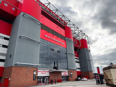 Manchester, İngiltere - 30 Eylül 2025: Manchester 'daki modern stadyum dışı kırmızı paneller, gri sütunlar, cam giriş, dramatik gökyüzü.