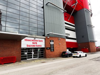 Manchester, İngiltere - 30 Eylül 2025: Tuğla ve metal cepheli modern stadyum kompleksi, Manchester Salford Suites 'in önünde park edilmiş arabalar.
