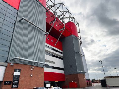 Manchester, İngiltere - 30 Eylül 2025: Kırmızı paneller, gri metal kaplama ve dramatik bir gökyüzü içeren Manchester Old Trafford Stadyumu