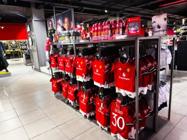 Manchester, İngiltere - 30 Eylül 2025: Bright Manchester mağazası modern bir perakende alanında kırmızı formalar ve takım ürünleri sergiliyor.