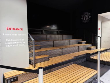 Manchester, İngiltere - 30 Eylül 2025: Manchester, İngiltere 'de modern bir stadyumda oturmakta olan Bleacher, ahşap basamaklar, metal örgüler ve öne çıkan bir giriş tabelasıyla donatılmıştır..