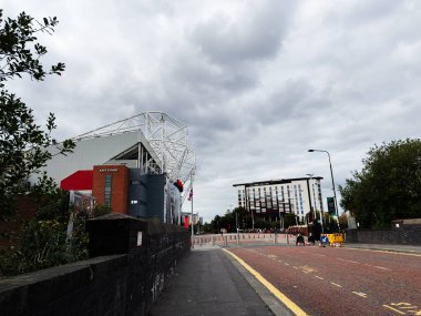 Manchester, İngiltere - 30 Eylül 2025: Manchester 'da geniş bir cadde tuğla ve cam yapısı olan modern bir stadyuma çıkıyor.