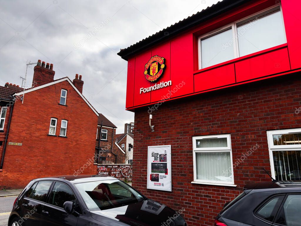 Manchester, UK - September 30, 2025: Red brick Manchester United Foundation building with crest; street scene featuring parked cars in the UK.