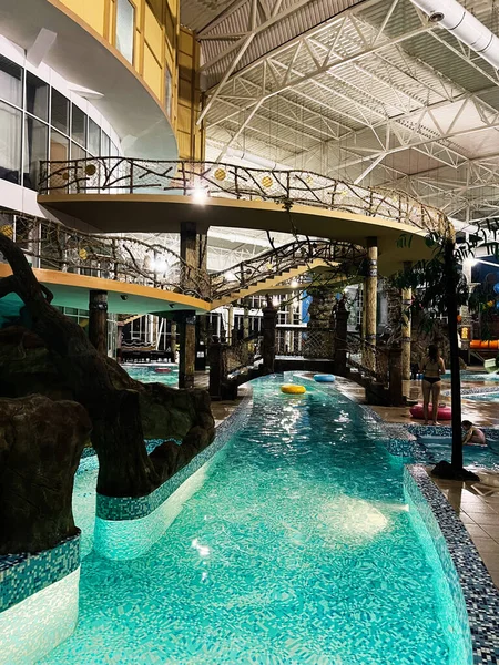 Khmelnytsky, Ukrayna - 10 Kasım 2025: Sarmal turkuaz havuzlu kapalı su parkı, köprüler ve uzay keyfini çıkaran konuklar.