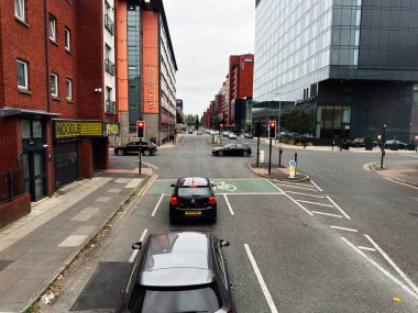 Manchester, İngiltere - 30 Eylül 2025: Manchester 'da trafik, bisiklet, kırmızı tuğla ve cam ofislerin yer aldığı sokak manzarası.