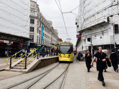 Manchester, İngiltere - 30 Eylül 2025: Manchester 'da inşaat yakınlarındaki işlek bir caddede yayalar ve müşterileri olan sarı bir tramvay.