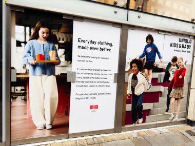Manchester, İngiltere - 30 Eylül 2025: Manchester 'da bir kız içki servisi yaparken Uniqlo mağazasının vitrininde çocuklar için moda gösterisi.