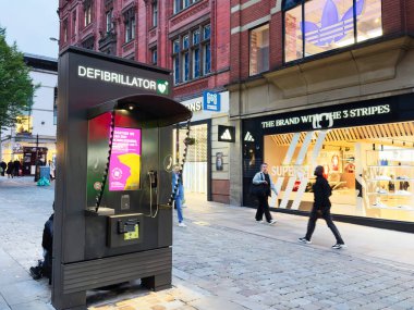Manchester, İngiltere - 30 Eylül 2025: Manchester 'da bir defibrilatör büfesi ve moda mağazalarının yer aldığı şehir caddesi.
