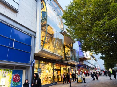 Manchester, İngiltere - 30 Eylül 2025: Manchester 'da canlı kentsel alışveriş alanı cam mimarisi, müşteriler ve sıcak mağaza önü ışıklandırması.