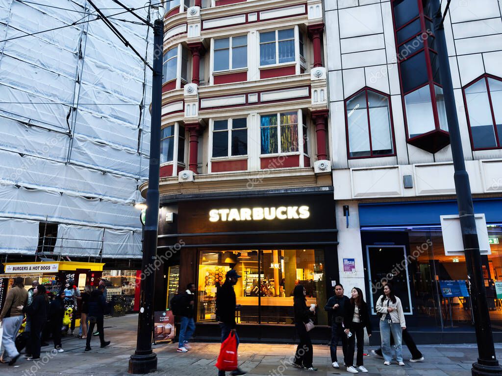 Manchester, UK - September 30, 2025: Bright Starbucks on a busy Manchester street among historic and modern buildings, with people nearby.