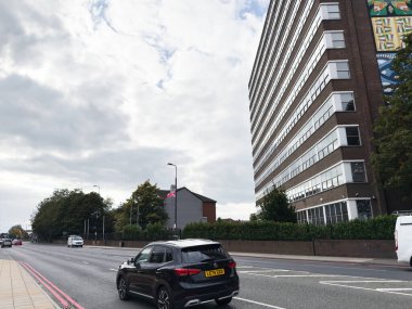 Manchester, İngiltere - 30 Eylül 2025: Manchester 'da yüksek binası, bayrağı ve araçları olan hareketli bir şehir caddesi.