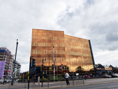 Manchester, İngiltere - 30 Eylül 2025: Yayalar ve trafiğin yoğun olduğu Manchester caddesinde modern bir bakır cephe ofisi bloğu.