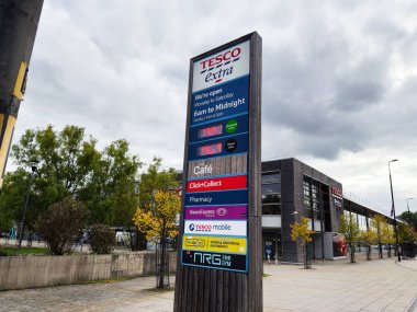 Manchester, İngiltere - 30 Eylül 2025: Manchester 'da yüksek tabelalı, ağaçlı ve bulutlu gökyüzü olan bir Tesco mağazasının dış görünümü.