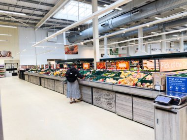 Manchester, İngiltere - 30 Eylül 2025: Bir tüketici bugün organize meyve ve sebze vitrinleriyle parlak bir süpermarkette taze ürünlere göz atıyor.