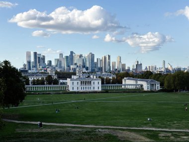 Londra, İngiltere - 22 Eylül 2025: Tarihi yapıları ve modern cam kulelerin uzak Londra silueti ile genişleyen yeşil park. Greenwich Parkı