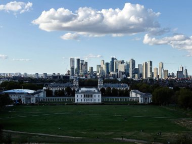 Londra, İngiltere - 22 Eylül 2025: Londra 'nın panoramik manzarası Greenwich tarihi binalarının arkasındaki modern gökyüzü ve geniş yeşil bir park.