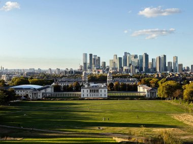 Londra, İngiltere - 22 Eylül 2025: Yeşil Greenwich Park önplanı ve tarihi kampüs binaları ile Londra 'nın ufuk çizgisinin geniş bir görüntüsü.