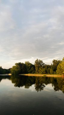 Güney Illinois 'deki sakin göl sahnesinde, alacakaranlıkta ağaç kaplı kıyı ve ayna yansımaları var..