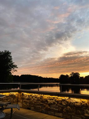 Güney Illinois 'de sıcak taş aydınlatma ve açık havada oturma ile sakin bir göl üzerinde altın gün batımı.