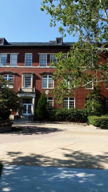 Kırmızı tuğlalı Güney Illinois Üniversitesi Carbondale binası beyaz pencereli, yeşillikli ve güneşli kampüs yolu.