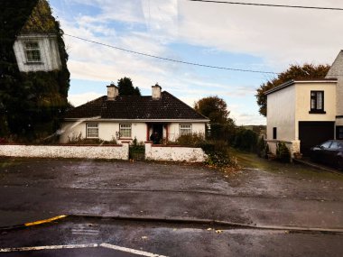 Longford, İrlanda - 21 Ekim 2025: Beyaz bir kulübe, çit ve nemli bir sokakta modern bir ev içeren antika bir İrlanda manzarası.