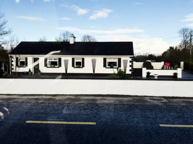 Longford, İrlanda - 21 Ekim 2025: Mavi gökyüzünün altında siyah süslemeli ve sade bahçeli temiz bir İrlanda kır evi.