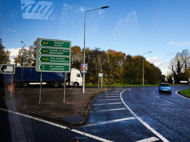 Edgeworthstown, İrlanda - 21 Ekim 2025: Yeşil yol işaretleri İrlanda 'da mavi bir arabanın yanındaki ıslak kavşağı gösteriyor.