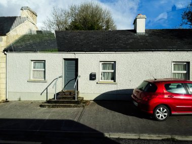 Edgeworthstown, İrlanda - 21 Ekim 2025: Mavi bir ön kapısı, beyaz duvarları, basamakları ve parlak bir gökyüzünün altında park etmiş kırmızı bir arabası olan küçük bir İrlanda evi..