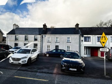 Curraghmore, İrlanda - 21 Ekim 2025: İrlanda 'da birden fazla araba, gri ve beyaz evler ve bir trafik işaretinin yer aldığı yerleşim yeri.
