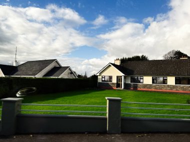 Curraghmore, İrlanda - 21 Ekim 2025 Tek bir aile evi, yeşil çimenler, mavi gökyüzü ve sakin bir sokak olan sakin bir İrlanda banliyö sahnesi.
