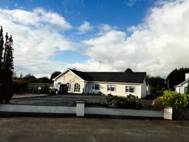 Curraghmore, İrlanda - 21 Ekim 2025: Açık gökyüzü altında, garaj yolu, beyaz duvarlar ve iyi korunmuş bahçesi olan güneşli bir İrlanda evi.