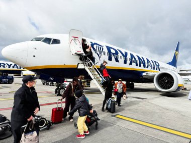 Dublin, İrlanda - 21 Ekim 2025: Bavulu ve pusetli yolcular bulutlu gökyüzünün altında Dublin havaalanında bir Ryanair uçağına biniyorlar.