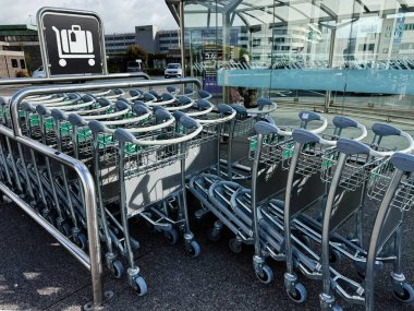 Dublin, İrlanda - 21 Ekim 2025: Dublin 'deki yolculara hazır cam bir havaalanı girişinin yakınındaki organize metal tramvaylar.