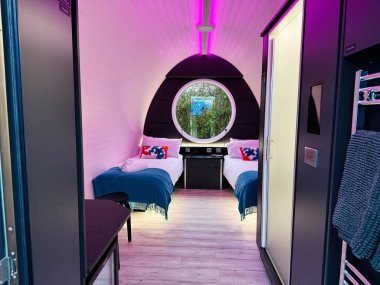 Knock, Ireland - October 22, 2025: Cozy twin bedroom in a modern hotel with round window, purple glow, and soft bedding.