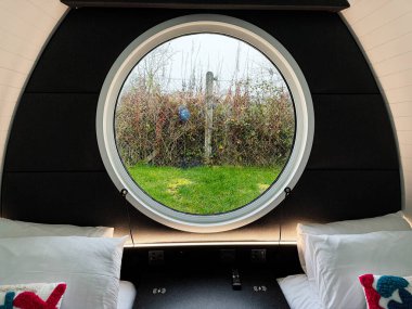 Tık, İrlanda - 22 Ekim 2025 Tak İrlanda 'da yeşil bir bahçe çerçeveli dairesel bir pencerenin yer aldığı rahat bir yatak odası sahnesi.