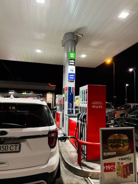 Krakow, Polonya - 25 Ekim 2025: Gece Orlen benzin istasyonu sahnesi pompada beyaz SUV, parlak gölgelik ışıklar ve yakınlarda hamburger tanıtımı.