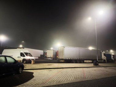 Krakow, Polonya - 07 Kasım 2025: Polonya gece sahnesi karavan, kamyonet ve sis dolu bir kamyon deposunu parlak lambaların altında gösteriyor.