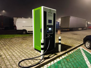 Krakow, Polonya - 07 Kasım 2025: Polonya gece sahnesi park alanında kablolar, kamyonlar ve kamyonlarla dolu yeşil bir EV noktasını gösteriyor.