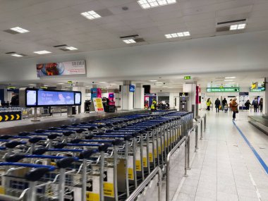 Manchester, İngiltere - 07 Kasım 2025: Manchester 'da yük arabaları, tabelalar ve seyahat için hazırlanan yolcular ile kalabalık havaalanı sahnesi.