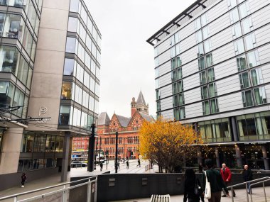 Manchester, İngiltere - 07 Kasım 2025: Modern ofisler Manchester 'da sonbahar rengi ve uzak kırmızı tuğla mimarisi ile bir yaya plazasını çevreledi.
