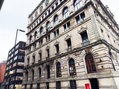 Manchester, İngiltere - 07 Kasım 2025: Kemerli camlar, taş işçiliği ve cadde boyunca parlak kırmızı bir posta kutusu bulunan büyük Manchester binası.