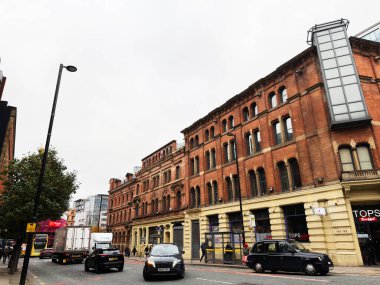 Manchester, İngiltere - 07 Kasım 2025: Manchester, İngiltere 'de kırmızı tuğla mimari, mağaza önü, trafik ve insanların yer aldığı şehir sahnesi.